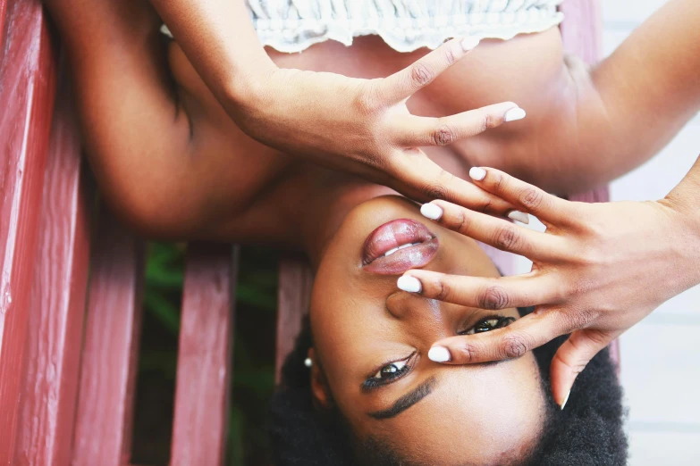 a close up of a person laying on a bench, by Dulah Marie Evans, trending on pexels, aestheticism, brown skin. light makeup, unclipped fingernails, looking up at camera, excitement