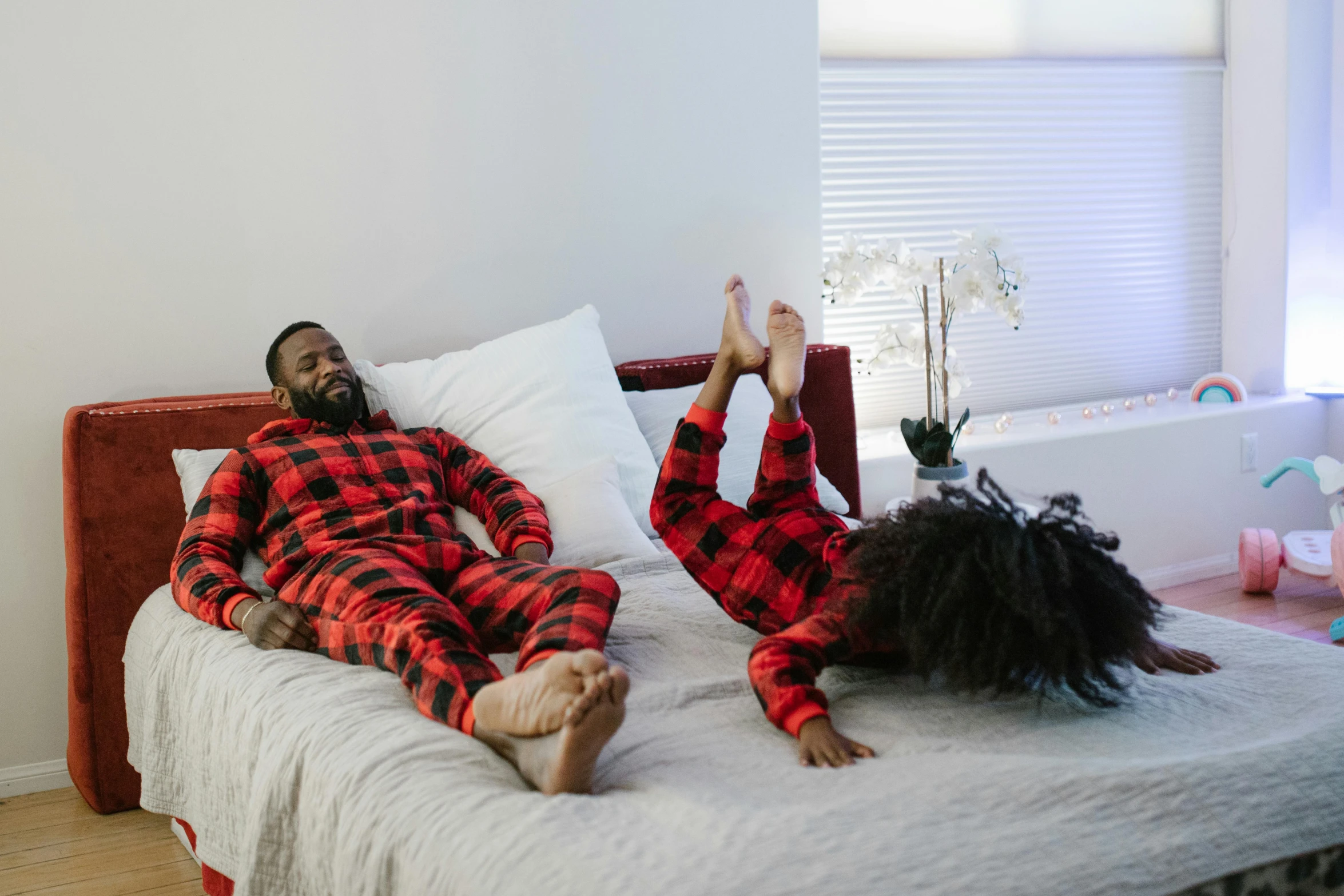 a couple of people laying on top of a bed, by Michael Gustavius Payne, pexels contest winner, black and red suit, dad energy, holiday season, wearing pajamas