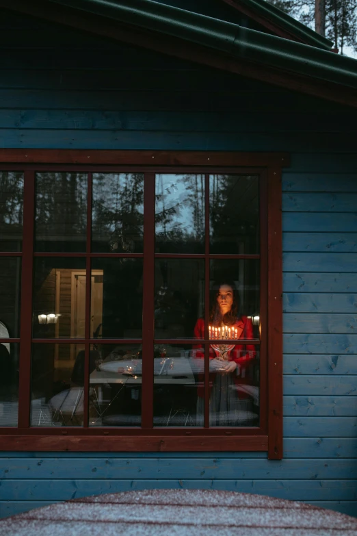 a person that is looking out of a window, by Eero Järnefelt, pexels contest winner, cabin lights, celebrating a birthday, reddish exterior lighting, front portrait