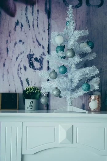 a white christmas tree sitting on top of a mantle, a colorized photo, by Elsa Bleda, shutterstock contest winner, white and teal metallic accents, white furniture, soft blue texture, white and purple