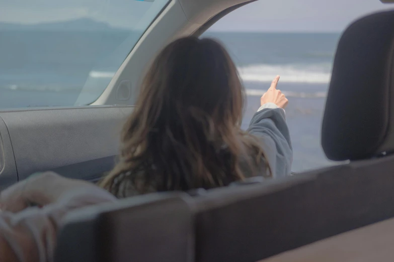 a woman sitting in the passenger seat of a car, unsplash, happening, middle finger, looking out at the ocean, leaving a room, distant - mid - shot