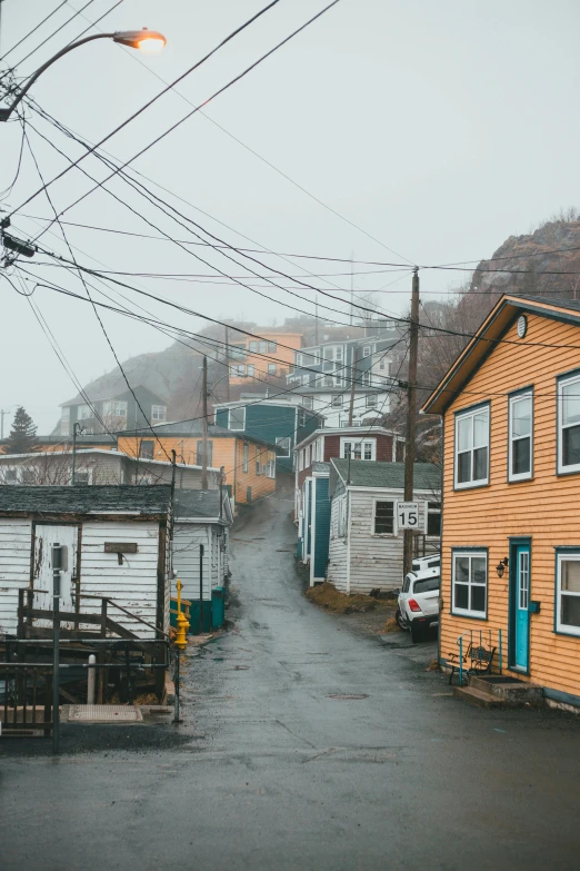 a yellow house sitting on the side of a road, by Jessie Algie, pexels contest winner, fishing town, under a gray foggy sky, a colorful, alley
