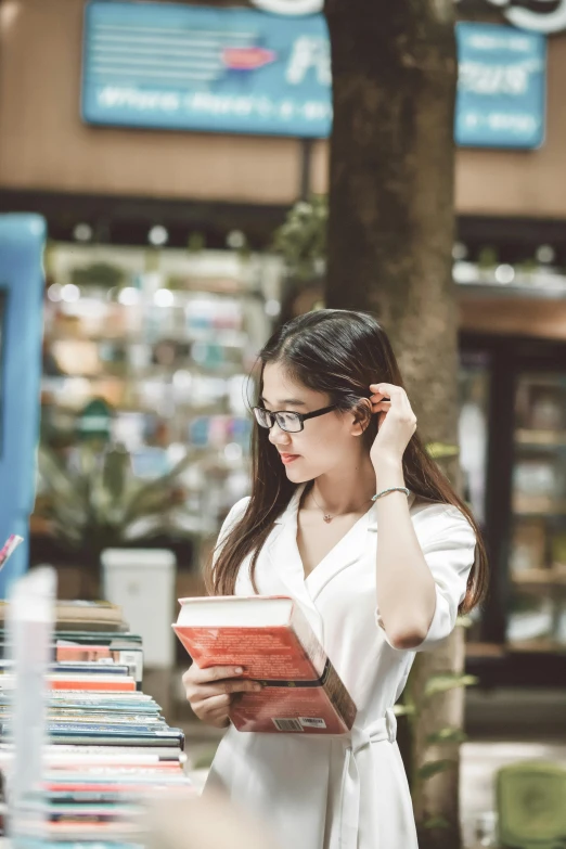 a woman in a white dress is reading a book, a cartoon, pexels contest winner, happening, at a mall, asian girl with long hair, reading glasses, gif