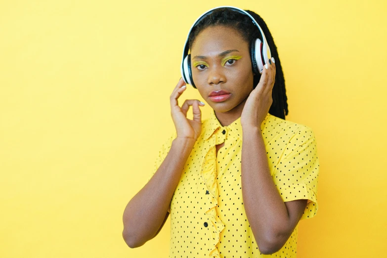 a woman holding a pair of headphones to her ear, inspired by Makoto Aida, trending on pexels, afrofuturism, colors: yellow, wearing a lemon, dynamic contrast, patterned clothing