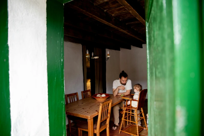 a man sitting at a table with a child, by Elsa Bleda, pexels contest winner, arts and crafts movement, inside of a cabin, arrendajo in avila pinewood, a green, farmhouse