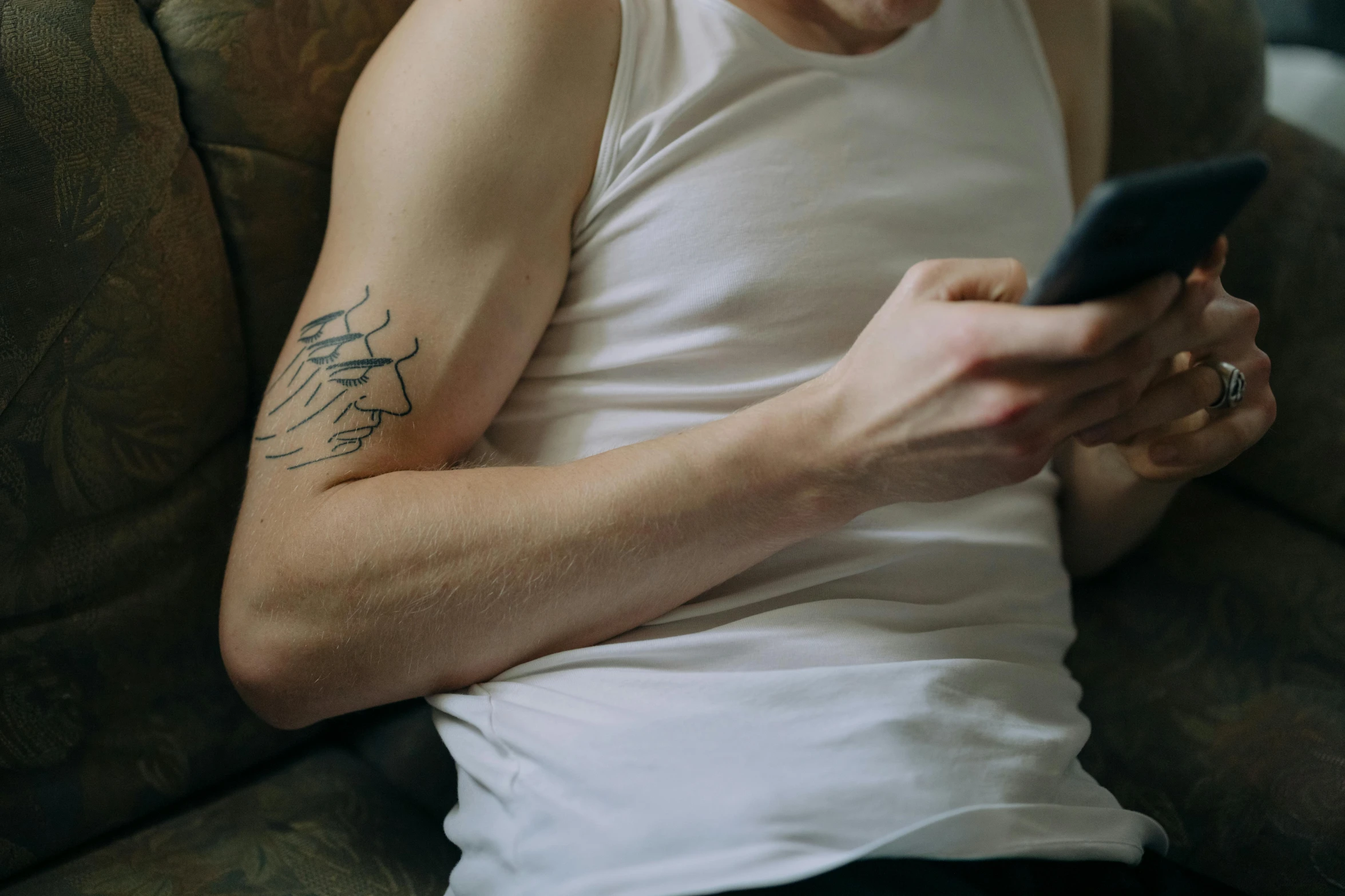 a man sitting on a couch holding a cell phone, a tattoo, by Adam Marczyński, trending on pexels, wearing a tanktop, from the elbow, extremely pale white skin, scribbled