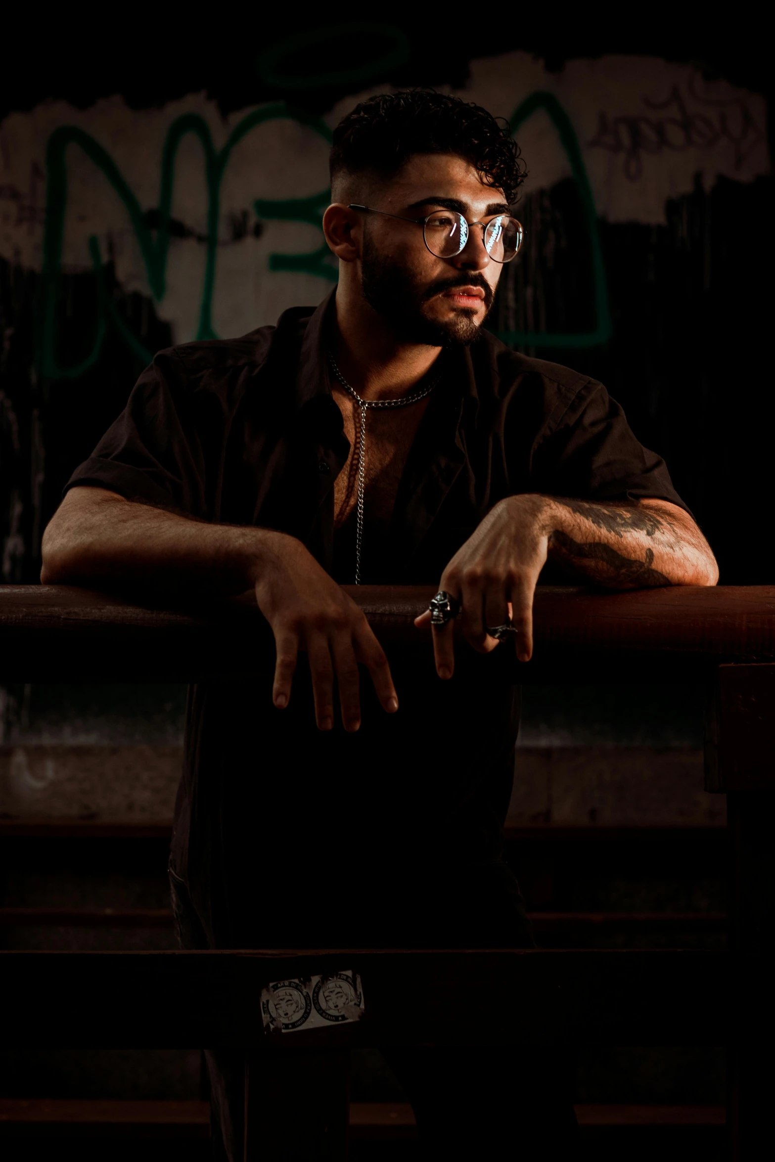 a man sitting on top of a wooden bench, an album cover, inspired by Camilo Egas, pexels contest winner, realism, with glasses and goatee, standing in a dark alleyway, black on black, attractive man