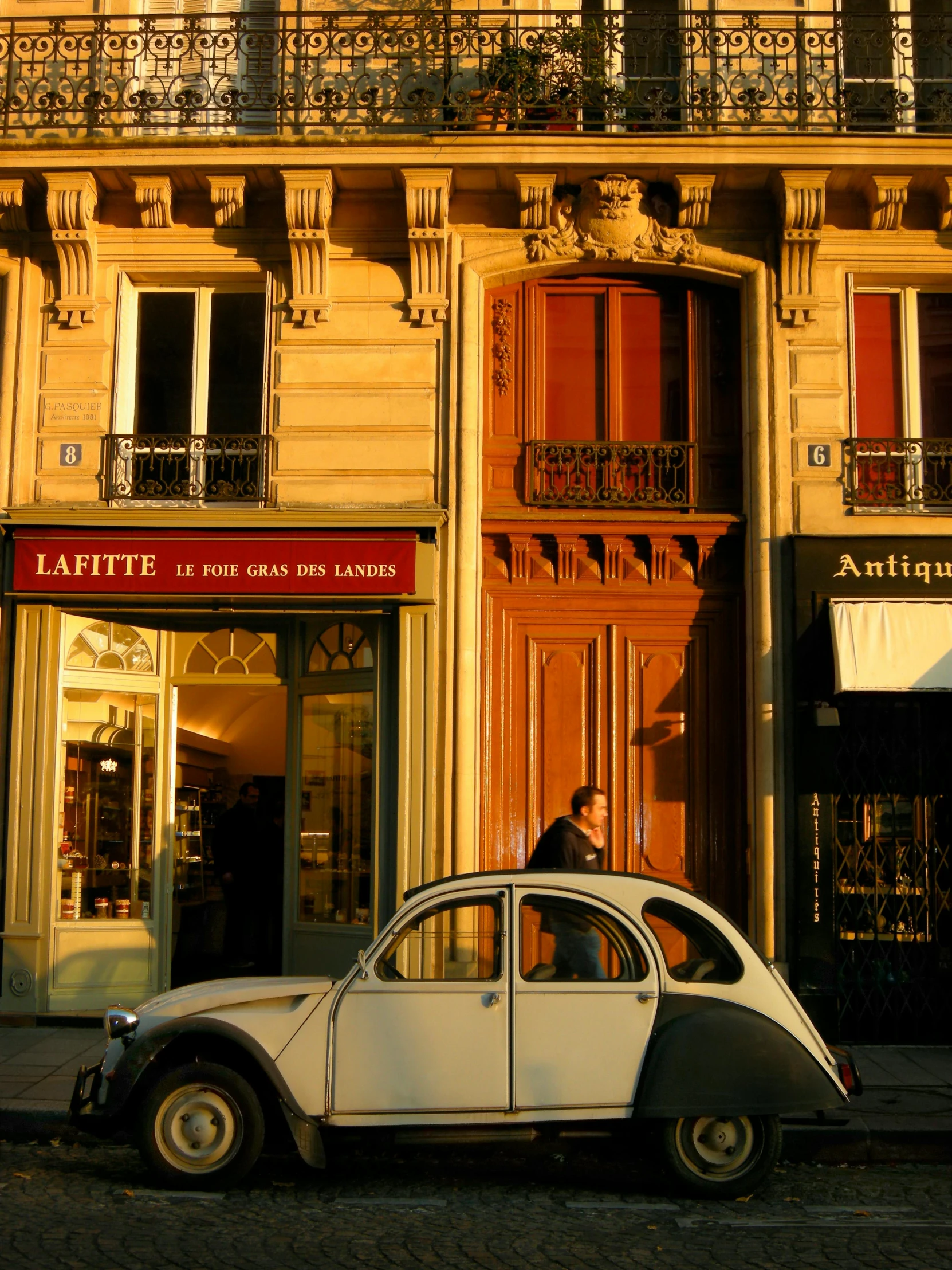 a small car is parked in front of a building, by Pierre Laffillé, cartier style, warmly lit, merchants, beetle