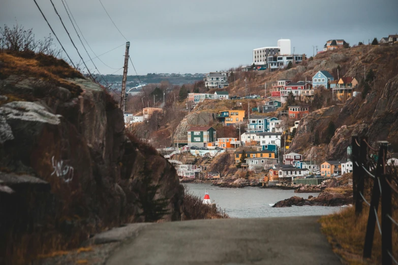 a road going down a hill next to a body of water, a photo, by Terese Nielsen, pexels contest winner, fishing village, habitat 6 7, brown, coastal cliffs