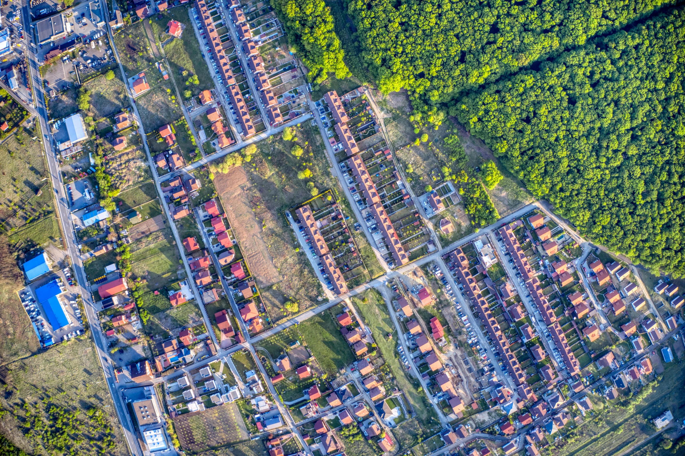 an aerial view of a small town surrounded by trees, by Adam Marczyński, shutterstock, ruined subdivision houses, coloured photo, wideangle, panels