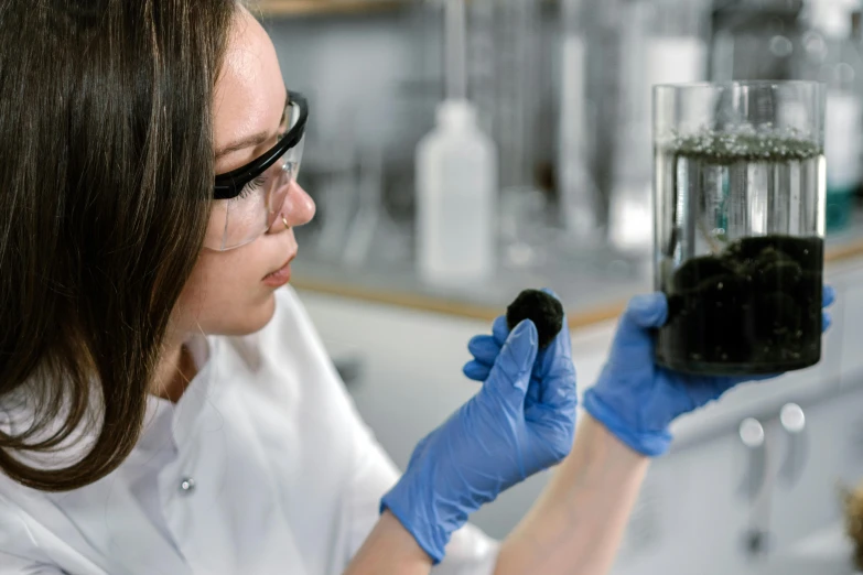 a woman in a lab coat holding a glass filled with dirt, ferrofluid oceans, avatar image, australian, profile image