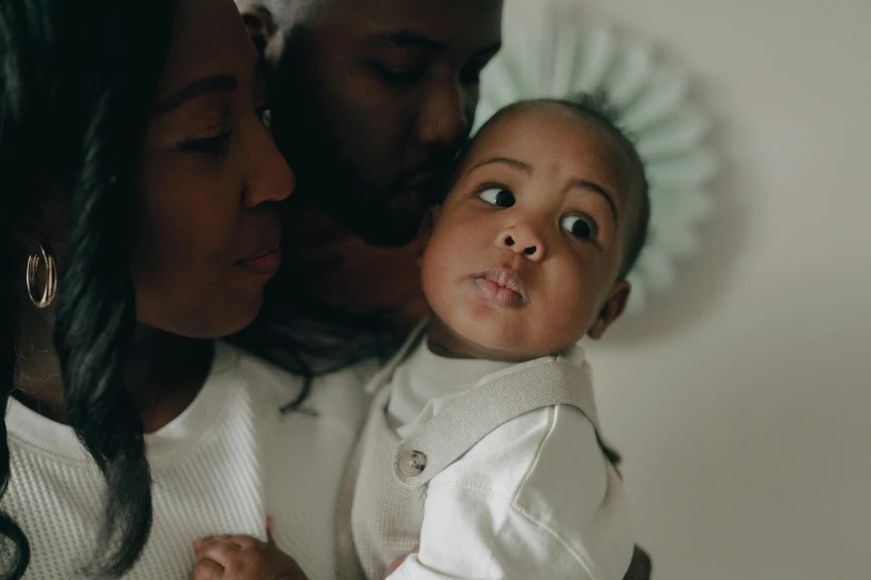 a close up of a person holding a baby, looking the camera, parents watching, dark skin, profile image