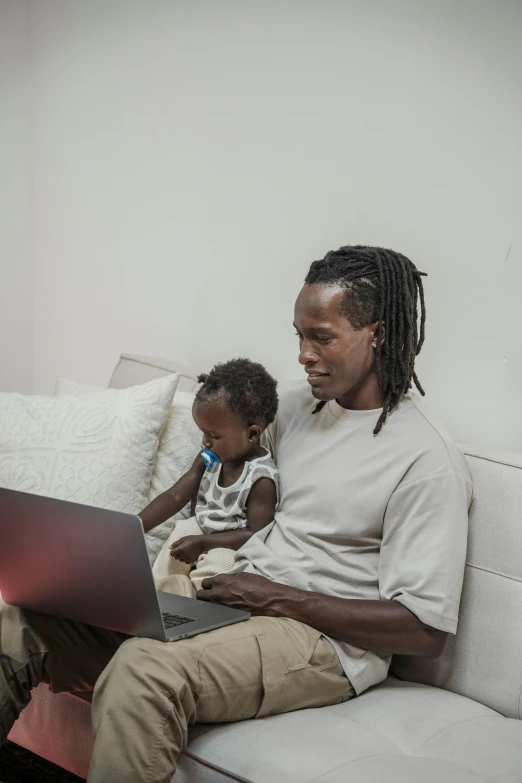 a man sitting on a couch using a laptop, by Michael Gustavius Payne, pexels contest winner, afrofuturism, father with child, a black man with long curly hair, low fi, with a long