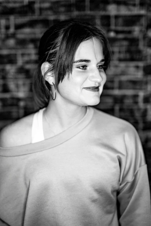 a woman standing in front of a brick wall, a black and white photo, inspired by Winona Nelson, lucy hale, smiling into the camera, epk, loosely cropped