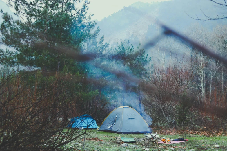 a couple of tents that are in the grass, by Lucia Peka, pexels contest winner, renaissance, smoke mist rain, retro effect, bushes in the background, hiking clothes