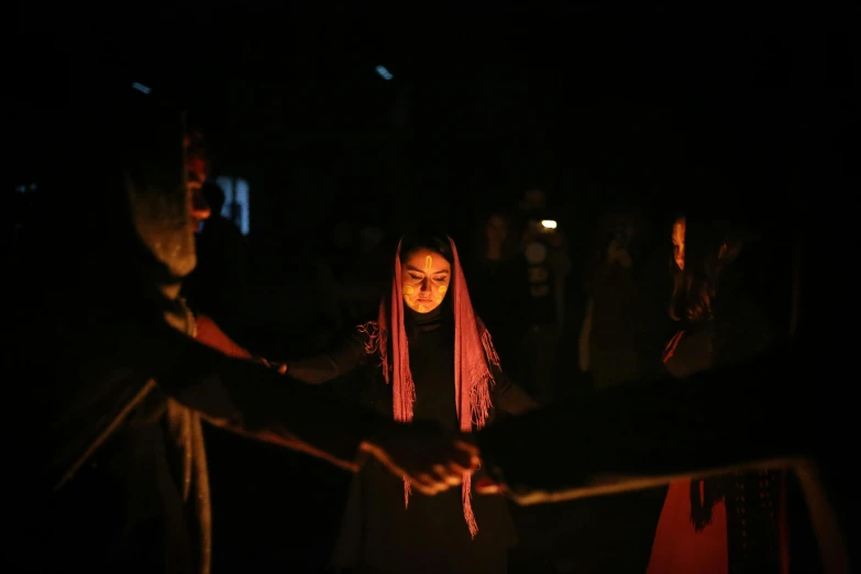 a group of people standing around a fire, a portrait, pexels contest winner, hurufiyya, fragile girl holding an arrow, candle lighting, sayem reza, hands pressed together in bow