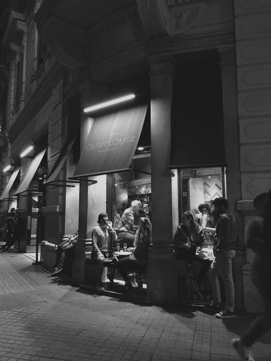 a black and white photo of a city street at night, a black and white photo, by Emma Andijewska, renaissance, people are eating, shop front, high quality image