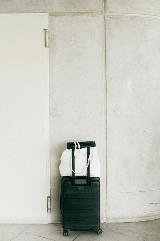 a suitcase sitting against a wall next to a door, unsplash, white and black clothing, background image, multiple stories, - 9