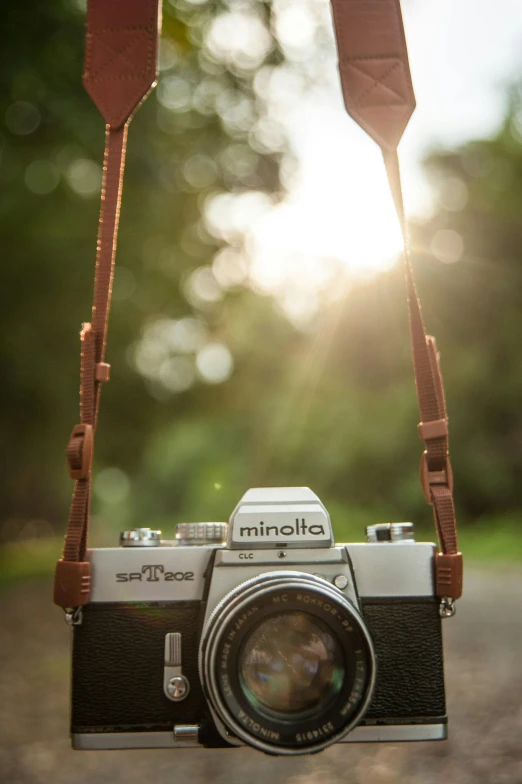 a camera with a strap hanging from it's neck, inspired by Elsa Bleda, unsplash contest winner, summer morning light, brown, medium wide front shot, konica minolta