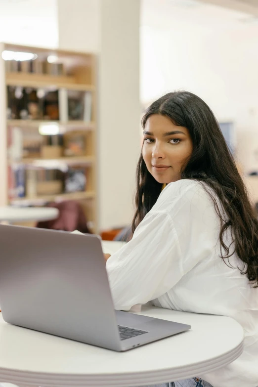 a woman sitting at a table with a laptop, trending on pexels, renaissance, young himalayan woman, standing in class, looking from shoulder, young with long hair