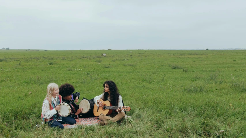 a group of people sitting on top of a lush green field, an album cover, by Jessie Algie, unsplash, hurufiyya, inuit heritage, women playing guitar, hollister ranch, 15081959 21121991 01012000 4k
