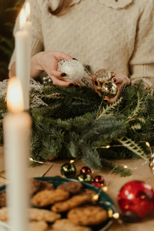 a woman decorating a christmas wreath on a table, by Julia Pishtar, trending on pexels, arts and crafts movement, cozy lights, ornament crown, tabletop, fully decorated