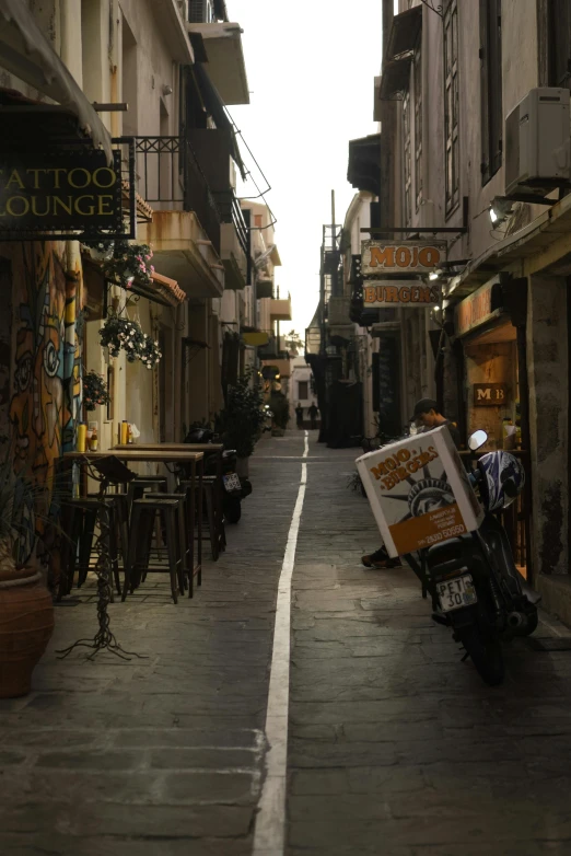 a motorcycle parked on the side of a narrow street, golden dawn, storefronts, taken in the early 2020s, square