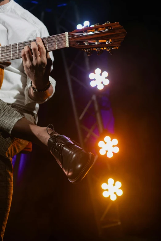 a man holding a guitar on top of a stage, pexels, wears brown boots, lights with bloom, dynamic closeup, flirting