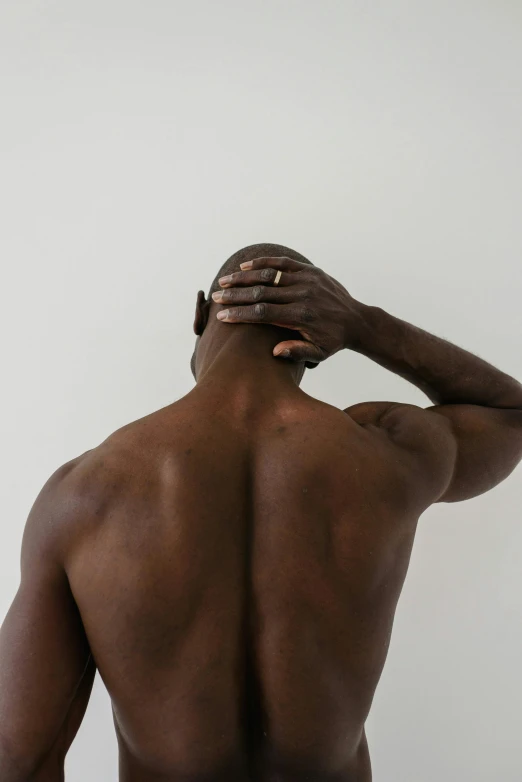 a man standing with his back to the camera, by Jessie Alexandra Dick, trending on pexels, light brown skin, vascularity, scratching head, plain background