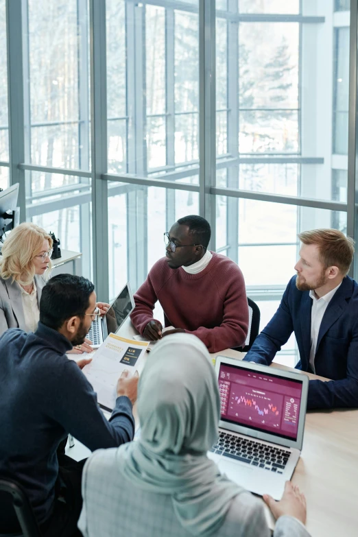 a group of people sitting around a table with laptops, in an office, varying ethnicities, thumbnail, selling insurance