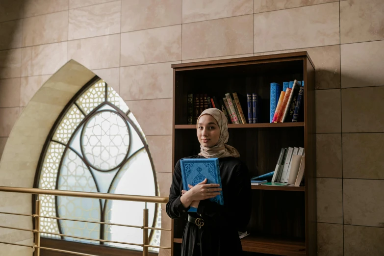 a woman standing in front of a bookshelf holding a book, hurufiyya, cybermosque interior, profile image, teaching