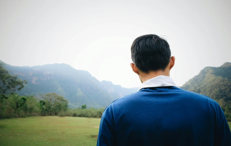 a man standing in a field with mountains in the background, inspired by Zhang Kechun, pexels contest winner, realism, back of head, wearing a dark blue polo shirt, looking outside, wondering about others