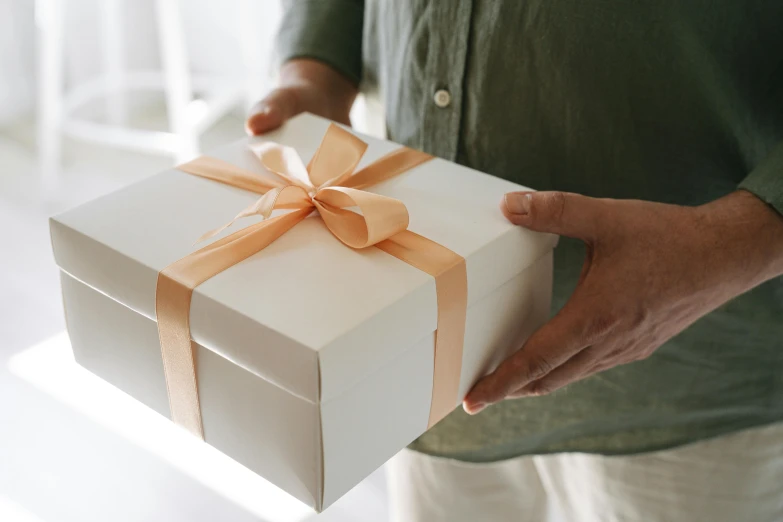 a man holding a white box with a orange ribbon, by Eden Box, pexels contest winner, private press, birthday wrapped presents, manly, soft white glow, thumbnail