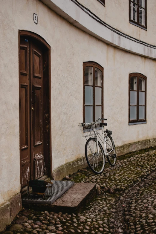 a bicycle parked next to a building on a cobblestone street, inspired by Wilhelm Marstrand, pexels contest winner, white and gold color scheme, doorway, iceland, brown
