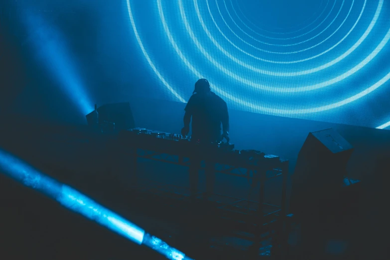 a person that is standing in front of some lights, blue room, dj set, circle forms, profile image