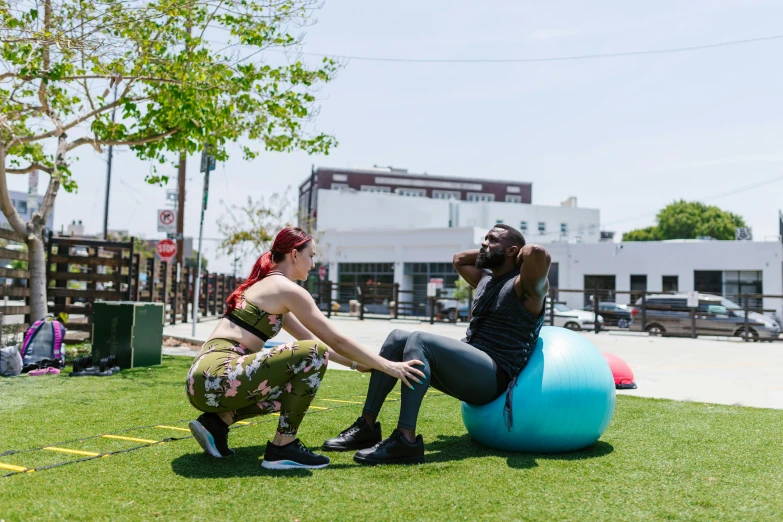 a couple of women sitting on top of a blue ball, mc ride, outside on the ground, dim dingy gym, jen atkin