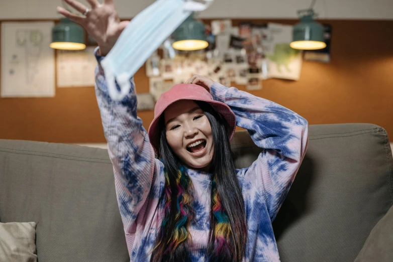 a woman sitting on a couch with her hands in the air, a portrait, inspired by Kim Jeong-hui, pexels contest winner, she is wearing streetwear, happy trippy mood, wearing a cute hat, avatar image
