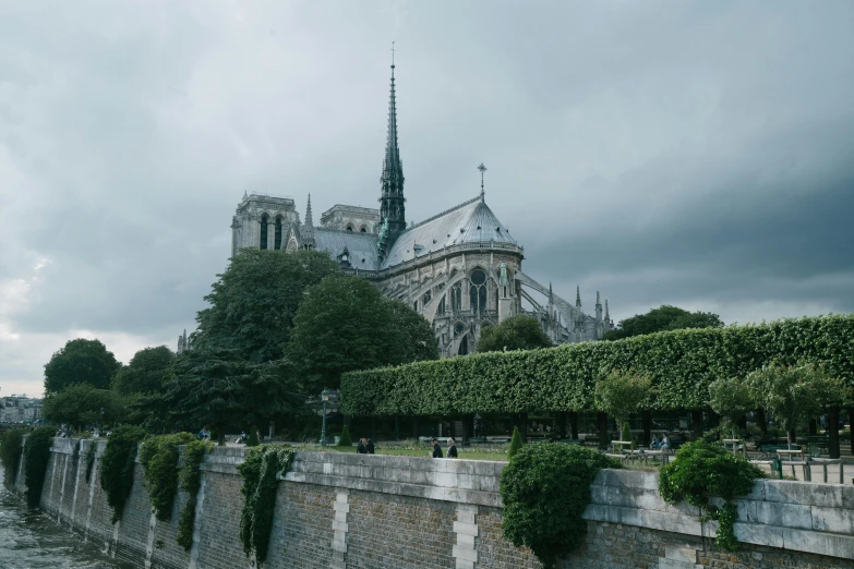 a large building sitting on the side of a river, pexels contest winner, paris school, gothic cathedral, grey cloudy skies, the city is full of green plants, 2 0 2 2 photo