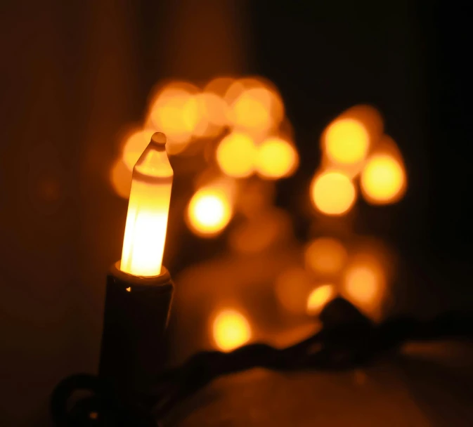 a lit candle sitting on top of a table, string lights, window lights, electric orange glowing lights, bokeh photograph