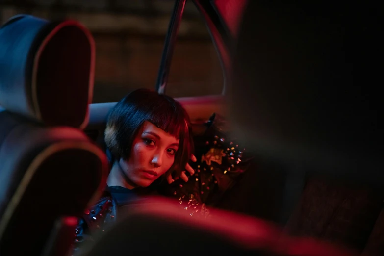 a woman sitting in the back seat of a car, inspired by Nan Goldin, realism, ornamental gothic - cyberpunk, dior campaign, red and cinematic lighting, kiko mizuhara