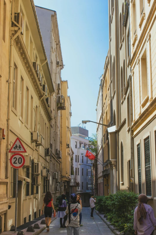 a group of people walking down a narrow street, a picture, monaco, traffic signs, beige, midday photograph