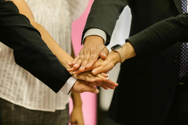 a group of people putting their hands together, by Arabella Rankin, pexels contest winner, elegantly dressed, hip corporate, holding a staff, holding each other