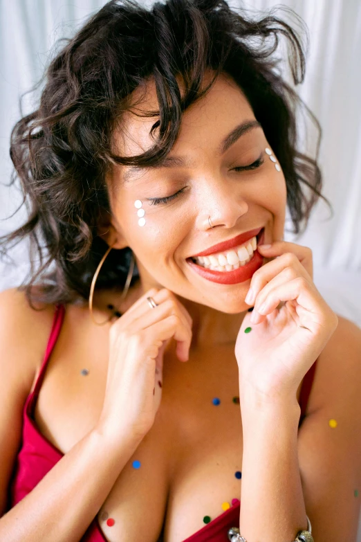 a woman sitting on top of a bed covered in confetti, trending on pexels, antipodeans, smiling soft vibrant lips, mixed race woman, red jewelry, left eye stripe