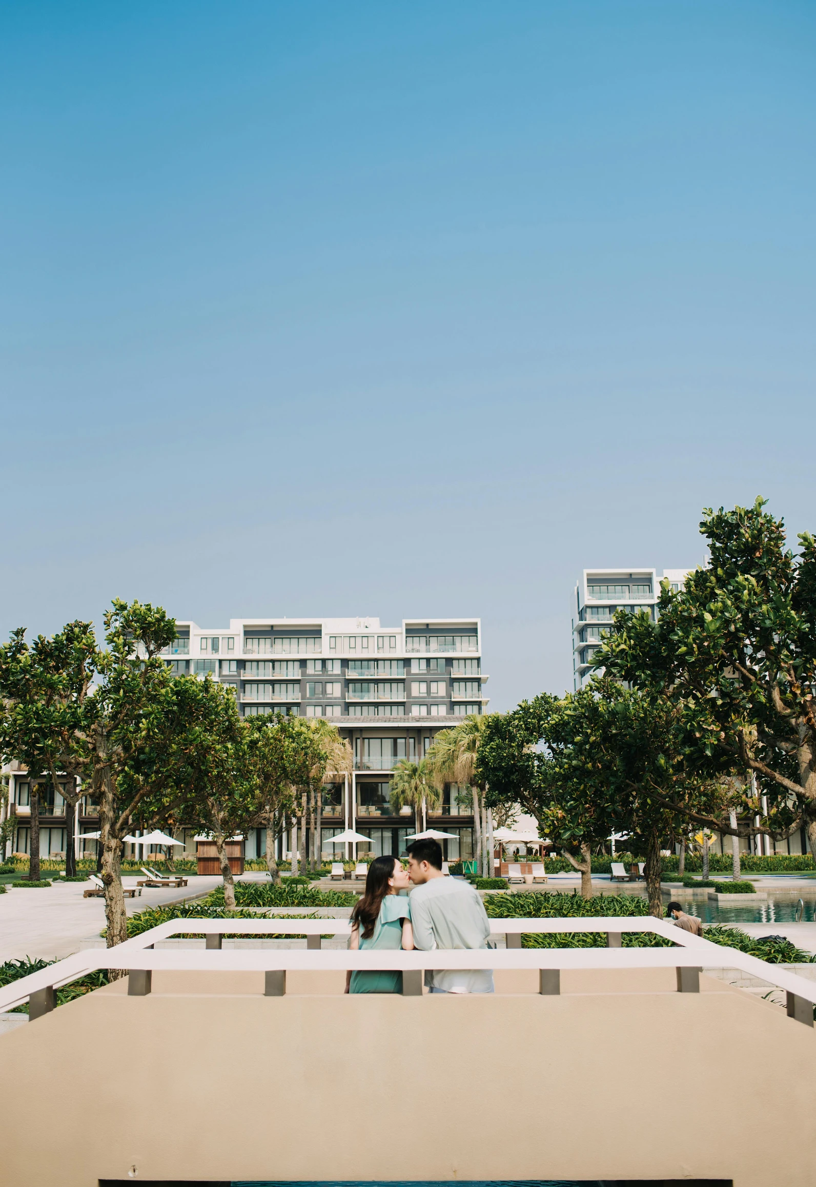 a couple standing next to each other in front of a building, in a beachfront environment, honeycomb halls, phuoc quan, square