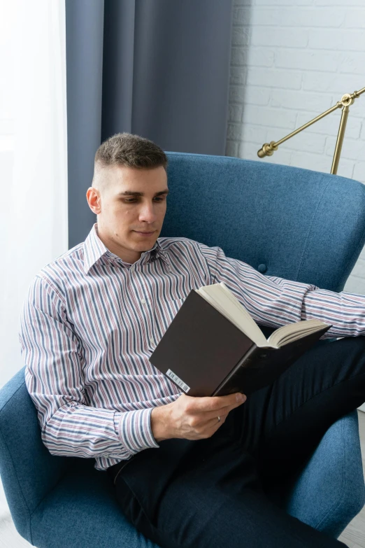 a man sitting in a chair reading a book, wearing business casual dress, lgbtq, russian academic, christian