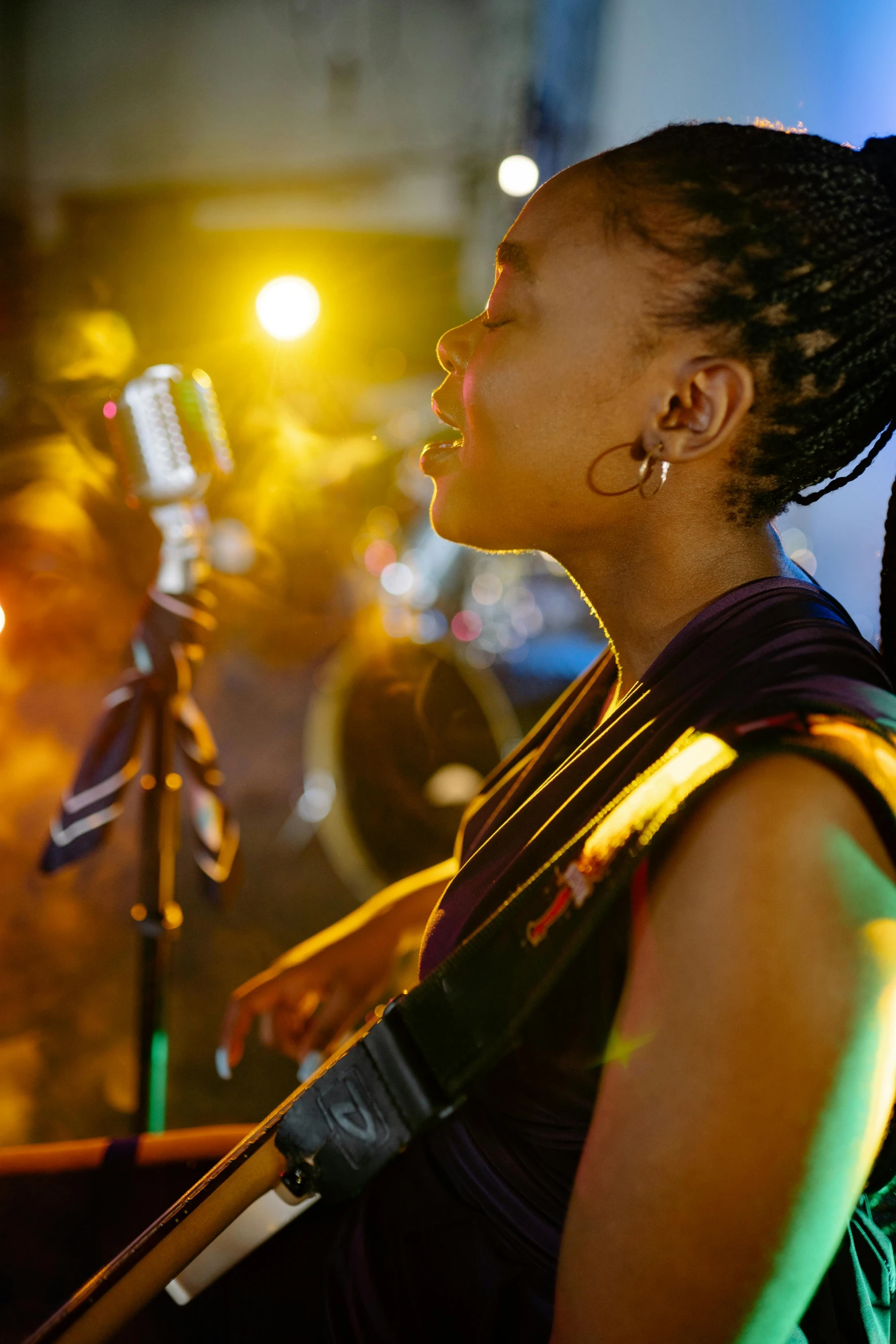 a woman playing a guitar in front of a microphone, by Leo Michelson, pexels, afrofuturism, summer festival night, profile image, multiple stories, taken in the late 2010s