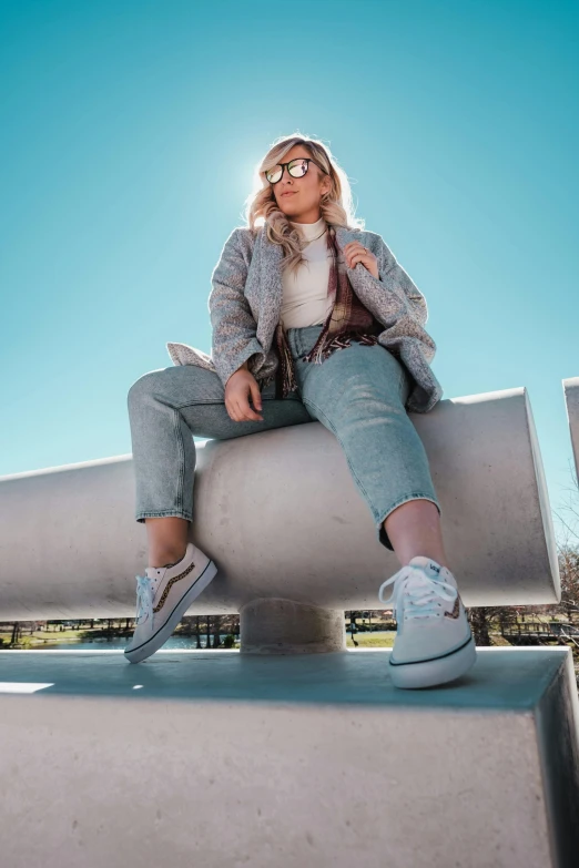 a woman sitting on top of a cement wall, trending on pexels, an aviator jacket and jorts, pastel blue, shot on gopro9, sitting on a park bench