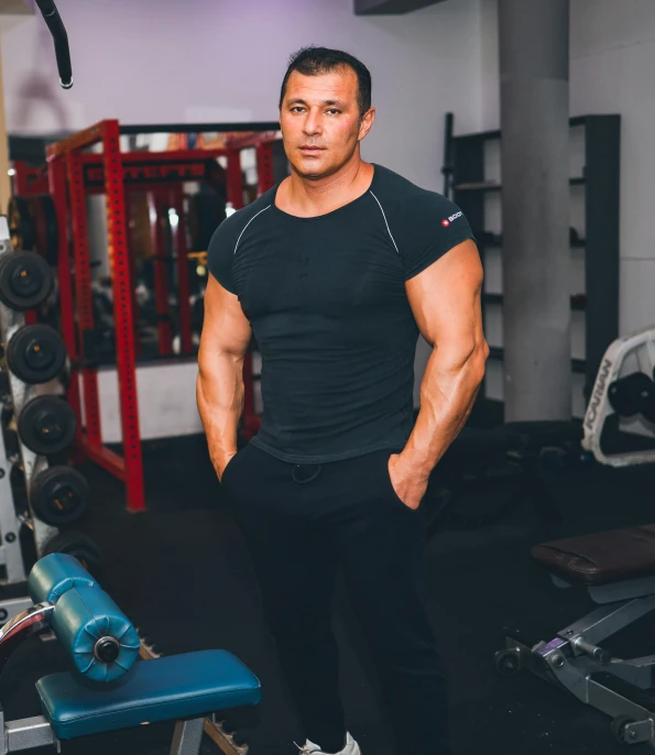 a man standing next to a bench in a gym, by Adam Marczyński, ernest khalimov body, edin durmisevic, profile image