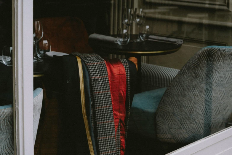 a chair sitting in front of a window next to a table, by Emma Andijewska, trending on unsplash, black and red tuxedo, tartan scarf, gentleman's club lounge, several layers of fabric