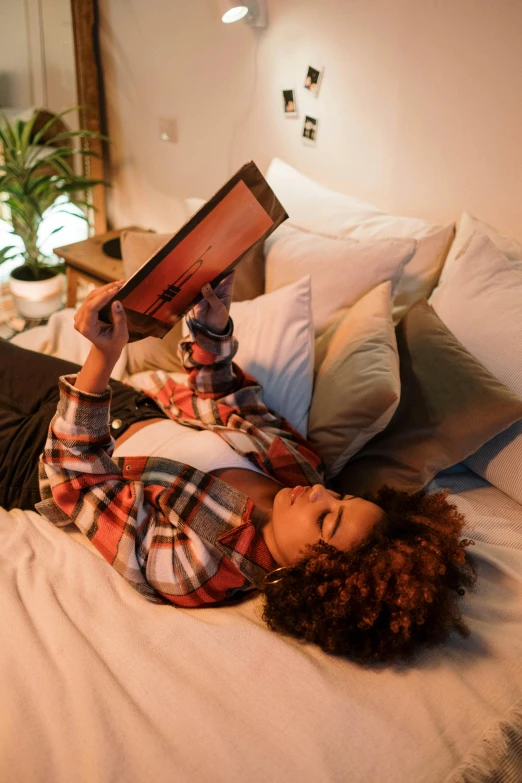 a woman laying on a bed reading a book, happening, ashteroth, using a magical tablet, lgbtq, evenly lit